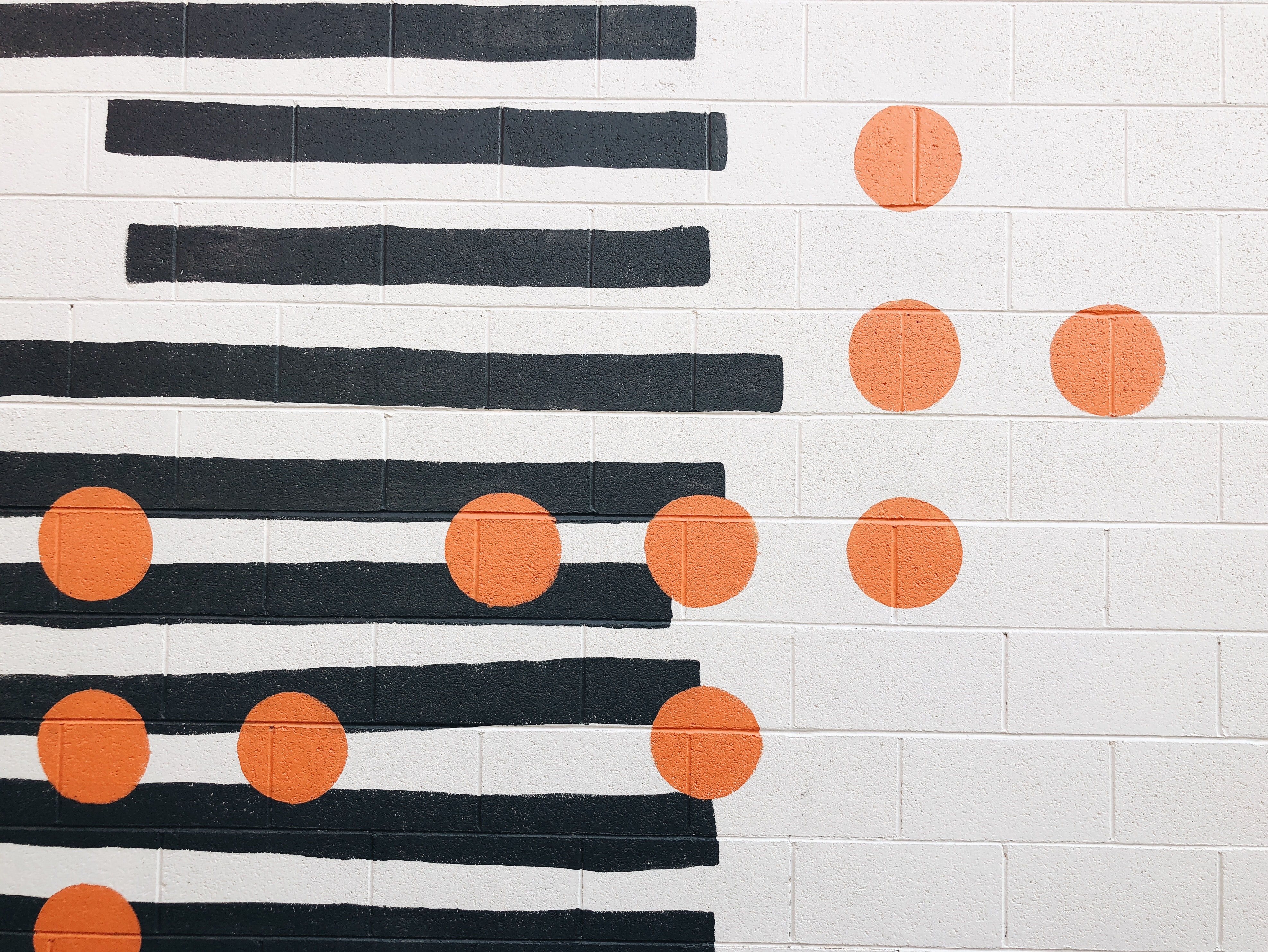 Black horizontal lines behind orange circles on a white block wall